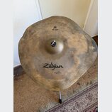 Kovový činel s nepravidelným, vlnitým okrajem a matným, patinovaným povrchem. Na povrchu jsou čitelné nápisy „fx RAW CRASH“ a logo „Zildjian“. V prav…