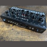 Černý syntezátor s nápisem BASSLINE a logem erica synths. Přístroj má řadu černých otočných ovladačů, několik přepínačů a bílé popisky funkcí. Na zad…
