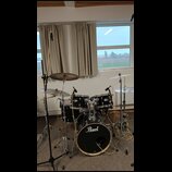 Černá bicí souprava značky Pearl s kovovým hardwarem. Sestává z basového bubnu s logem Pearl, dvou tomů, jednoho floor tomu a tří činelů. Nástroje js…
