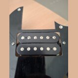Fotografie detailně zobrazuje černý humbucker snímač s dvěmi řadami magnetických pólů osazených šrouby a kolíky. Snímač je umístěn v černém plastovém…