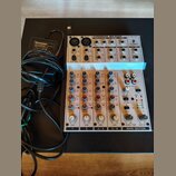 Bílý mixážní pult s nápisem EURORACK MX 602A a logem BEHRINGER. Zařízení obsahuje čtyři vstupní kanály s ovládacími prvky EQ, AUX a PAN, vpravo je MA…