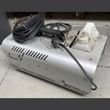 Stříbrný kouřový stroj z kovu s bílou plastovou nádržou na tekutinu. Na přístroji jsou nápisy „Antari“, „Z-1200 SMOKE FOGGER“ a „Z 1200 series“. Povr…