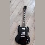 Černá elektrická kytara s dvojsekyrou v tvaru SG. Na hlavě hmatníku je bílý nápis Urville a zlatý znak. Nástroj má dva humbuckery, stříbrný most s ko…