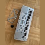 Světle šedý elektronický klavír s plastovým korpusem a bílo-černými klávesami. Na přístroji jsou viditelné nápisy „128 TONE“ a „128 VOICE“, uprostřed…