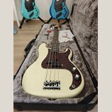 Bílá elektrická basová kytara v černém polotvrdém kufru s šedým polstrováním. Nástroj má hnědý želvový pickguard a chromovaný most. Na hlavě krku je…