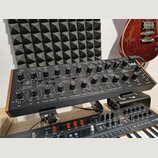 Černý analogový syntetizátor v dřevěném rámu s množstvím ovládacích knoflíků a přepínačů. V pravém horním rohu je bílé logo Korg. Na panelu jsou čite…