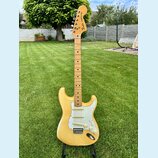 Elektrická kytara s žlutým trupem, bílým pickguardem a hnedým javorovým hmatníkem. Na hlavě je vidět logo Fender a nápis STRATOCASTER. Nástroj má tři…