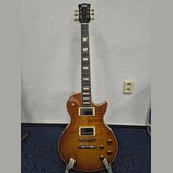 Elektrická kytara s trupem v barvě honey burst a hmatníkem s trapezoidními vložkami. Na hlavě je bílé logo FGN a nápis Classic. Nástroj má dva humbuc…