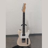 Elektrická kytara s bílým trupem, bílým pickguardem a hnědým hmatníkem. Na hlavě je viditelné logo Fender. Nástroj má dva snímače, jeden v pozici kob…