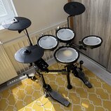 Elektronická bicí souprava černé barvy s bílými membránami. Na modulech a rámu je viditelný nápis Roland a na membránách označení V-Drums. Souprava o…