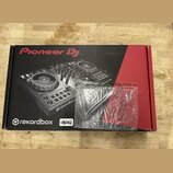 Kartonová krabice s obrázkem DJ kontroléru v černém a červeném provedení. Na krabici jsou nápisy Pioneer DJ, rekordbox a djay. Před krabicí leží průh…