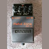 Černý efekt pedál s oranžovými nápisy Metal Zone a MT-2. Na spodní části je vyražené logo BOSS. Horní panel obsahuje čtyři ovládací knoflíky, červeno…