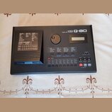 Černý digitální MIDI sekvencer s nápisem KAWAI Q-80 DIGITAL MIDI SEQUENCER. Zařízení má malý displej, ovládací tlačítka a vlevo slot pro diskety. Pov…