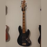 Černá elektrická basová kytara s černým pickguardem a hnedým hmatníkem. Na hlavě je viditelný nápis Fender JAZZ BASS. Nástroj vykazuje běžné známky p…