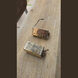 Dvě elektrické kytarové snímače typu humbucker v pozlaceném provedení. Snímač v horní části má hladký kryt s viditelnými šrouby, spodní snímač má kry…