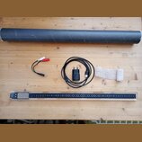 Fotografie zobrazuje dlouhý, úzký elektronický nástroj v průhledném plastovém krytu s černým vnitřním panelem. Na levé straně je vidět nápis "SOMA" a…