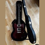 Tmavě červená elektrická kytara s tmavým hmatníkem v černém tvrdém kufru. Na hlavě nástroje je viditelné logo Gibson. Tělo kytary má dva humbuckery,…