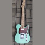 Světle zelená elektrická kytara typu Telecaster s javorovým hmatníkem a tmavě červeným šasi z vymyšleného perleťového plastu. Na hlavě je viditelné k…