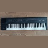 Černý digitální klávesový nástroj s bílými a černými klávesami. Na pravé straně ovládacího panelu je bílý nápis Roland JV-50 EXPANDABLE SYNTHESIZER.…