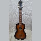 Akustická kytara s tmavě hnědým přechodem do žluté barvy (sunburst). Na hlavě je bílý nápis Framus. Nástroj vykazuje známky opotřebení, zejména v pod…