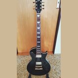 Černá elektrická kytara s tvarem singlecut a zlatým hardwarem. Na hlavě je bílé logo Ltd a svislý nápis EK-250. Nástroj má dva humbuckery s krémovými…