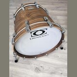 Kytlicový basový buben s dřevěným korpusem v hnědé barvě a bílým exponovaným koženem. Na koženě je černý nápis DRUM CRAFT a nad ním grafické logo. Bu…