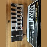 Stříbrný MIDI kontrolér s černými spínači a dvěma expresními pedály. Na přístroji je nápis FCB1010 MIDI FOOT CONTROLLER a na pedálech logo Behringer.…
