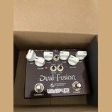 Tmavě hnědý kytarový pedál s bílými popisky a ovládacími knoflíky. Na povrchu je uveden název Dual Fusion, nápis Tom Quayle signature dual overdrives…