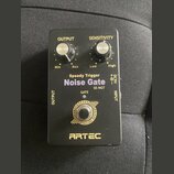 Černý efekt pedál s nápisy Speedy Trigger Noise Gate a SE-NGT. Na horní straně jsou dva ovládací knoflíky s popisky OUTPUT (Min, Max) a SENSITIVITY (…