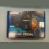 Fotografie znázorňuje krabici s produktem Shure GLX-D Digital Wireless Guitar Pedal. Na obalu je zobrazen černý bezdrátový pedál s červeným digitální…