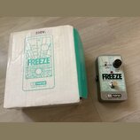 Na fotografii je efekt pedál v šedém kovovém provedení a jeho původní bílo-zelená krabice. Na pedálu i na krabici je uveden nápis FREEZE SOUND RETAIN…