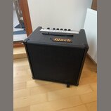 Černý basový kombozesilovač s texturovaným povrchem a černou ochrannou mřížkou. Na horní části je umístěno logo Markbass a úchyt pro přenos. Horní pa…