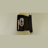 Černý úzký kufr, ve kterém je umístěn stříbrný mikrofon a srolovaný šedý kabel. Kabel je svázaný červeným plastovým stahovákem. V pravé části je přip…