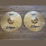 Dvě mosazné činely značky Zildjian s viditelným rakováním. Levý činel nese nápisy ZHT a Mastersound Hihat Bottom 13"/33 cm. Pravý činel má nápisy ZHT…