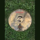 Kruhový činel z mosazného kovu s viditelným ručním kováním povrchu. V horní části je červený nápis Masterwork a pod ním menší text Hand Hammered Turk…