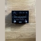 Černý efekt pedál s nápisy CUSTOM AUDIO ELECTRONICS a BOOST / OVERDRIVE. Na horní části jsou čtyři ovládací knoflíky s popisky BOOST (s rozsahem 0 dB…