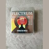 Balení kytarových strun v průhledném plastovém obalu. Na obalu je nápis PLECTRUM, kód AC210 a označení 12 STRING SET. V dolní části je uveden výrobce…