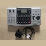 Stříbrošedý digitální nahrávací multitrack s nápisem ZOOM MRS-8 Natural Recording Studio. Zařízení obsahuje displej, ovládací knofíky, řadu posuvníků…