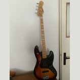 Elektrická basová kytara s trupem v barevném přechodu od žluté po tmavě hnědou a černým pickguardem. Na hlavě hmatníku je viditelné logo Squier. Hmat…