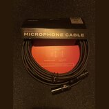 Černý mikrofonní kabel s konektory XLR, umístěný před svým originálním černým a červeným obalem. Na krabici jsou nápisy D'Addario, AMERICAN STAGE MIC…