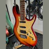 Elektrická kytara s trupem v červeno-žlutém sunburst provedení a hnědým hmatníkem. Nástroj má tři snímače (dvě jednosnívkové a jeden humbucker u koby…