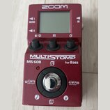 Vínový efekt pedál s displejem a třemi ovládacími knoflíky. Na horní části je bílé logo ZOOM, v prostřední části nápisy MULTISTOMP, MS-60B a for Bass…