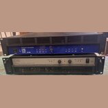 Dva rackové výkonové zesilovače naskládané na sebe. Horní zařízení je modré s černým horním krytem a nápisy PROFESSIONAL POWER AMPLIFIER, logo AG aku…