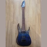 Elektrická kytara s modrým přechodovým lakem a viditnou strukturou dřeva na hranách. Na hlavě hmatníku je bílý nápis Ibanez. Nástroj má dva humbucker…