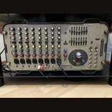 Šedý mixážní pult v černém transportním kufru. Na pravé straně je svisle napsáno logo Soundcraft a v dolní části nápisy GIGRAC 1000sc, GIG a combined…
