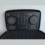 Černý DJ kontrolér Pioneer DJ model DDJ-FLX4 umístěný v černé polstrované přepravní brašně. Na přístroji jsou viditelné nápisy rekordbox a serato. Po…