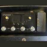 Černý efektový procesor s nápisem AMPERO Amp Modeler / Effects Processor. Zařízení má čtyři průhledné ovládací knofíky, dva zlaté knofíky s popisky V…