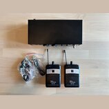 Černý bezdrátový systém pro in-ear monitoring. Sada obsahuje jeden hlavní vysílač a dva malé přijímače s anténami, z nichž oba mají bílý nápis „the e…