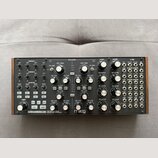 Stříbrný semi-modulární analogový syntetizátor s dřevěnou bočními stěnami. Na předním panelu je vlevo dole nápis SUBHARMONICON | SEMI-MODULAR ANALOG…