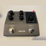 Šedý efekt pedál s černými ovládacími knoflíky a dvěma stoupacími spínači. Na zařízení jsou nápisy VLP-200 MULTI-TRACK SAMPLER, VALETON, LOOP 1 a LOO…
